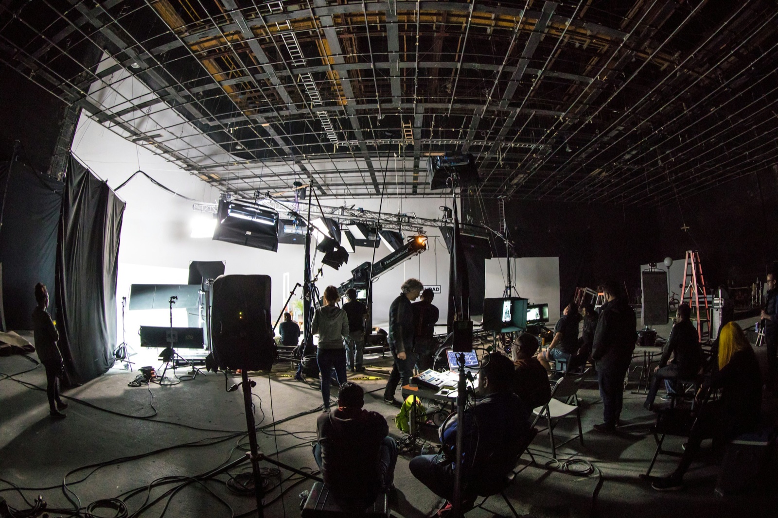Bastidores de um set de produção audiovisual, com câmeras, iluminação e equipe de filmagem